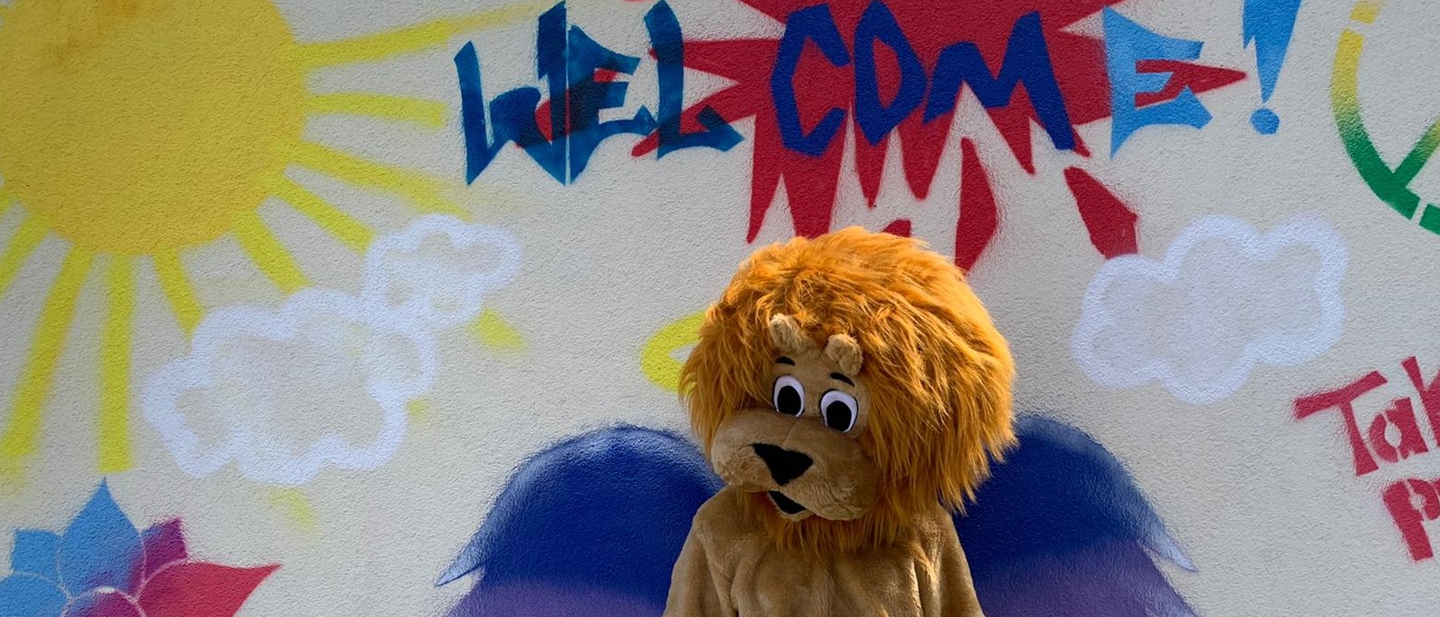 Das Leo-Maskottchen vor einem Welcome-Sign